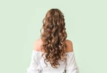 Quels sont les différents types de permanente ? femme de dos avec cheveux longs ondulés et permanente, fond vert pâle