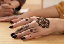 Peut-on utiliser du henné pendant la grossesse ? main avec henné traditionnel et vernis noir, bagues dorées sur table en bois