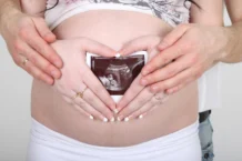 femme enceinte tenant une échographie et ses mains en cœur sur son ventre